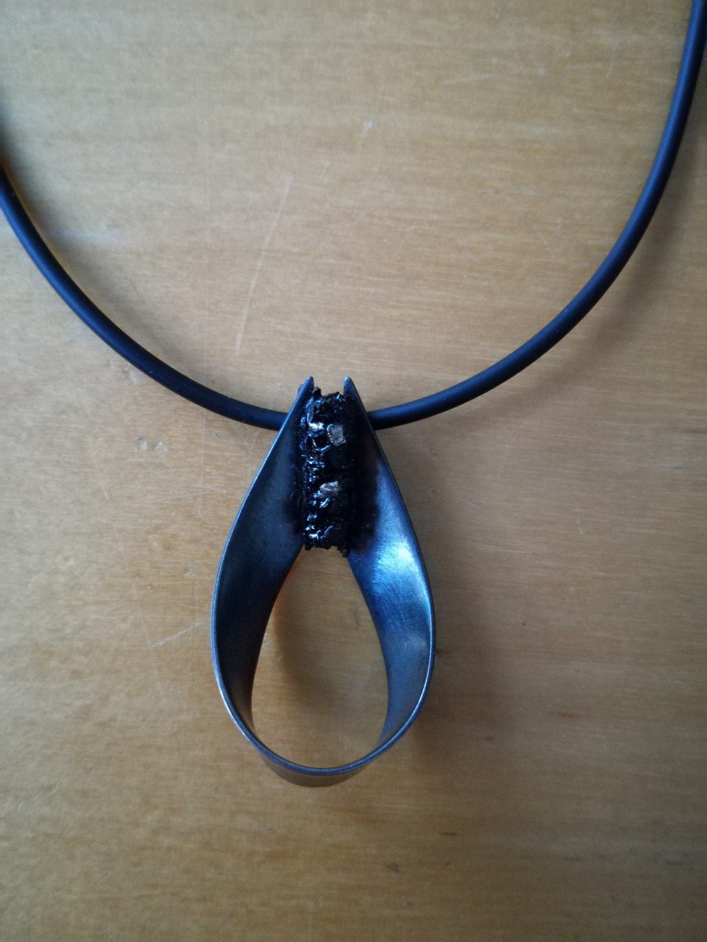 In zilver gesmeede zwarte druppel met koker van tourmalijn zwart afgewerkt met een caoutchouc collier.